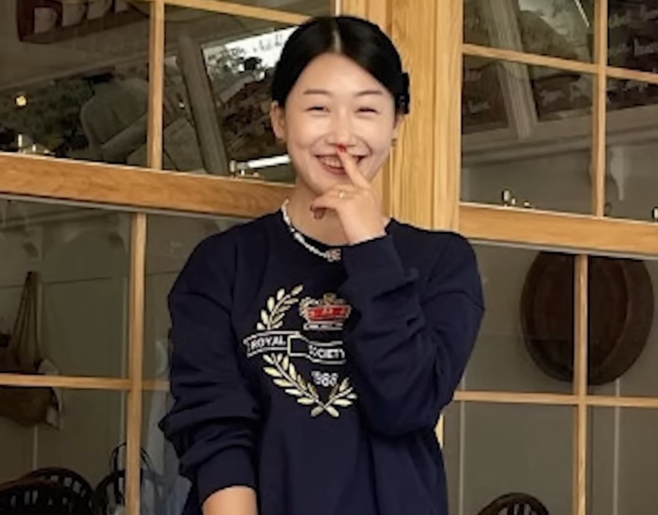 영숙이 남색의 박스티를 입고 한쪽 속을 입쪽으로 올리고 검지손가락을 입술에 갖다대고 이빨이 보이도록 환하게 웃고 있다.