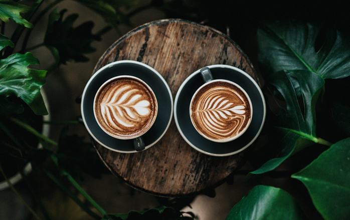 나무 받침 위에 놓여있는 예쁘게 장식된 커피 라떼 두 잔