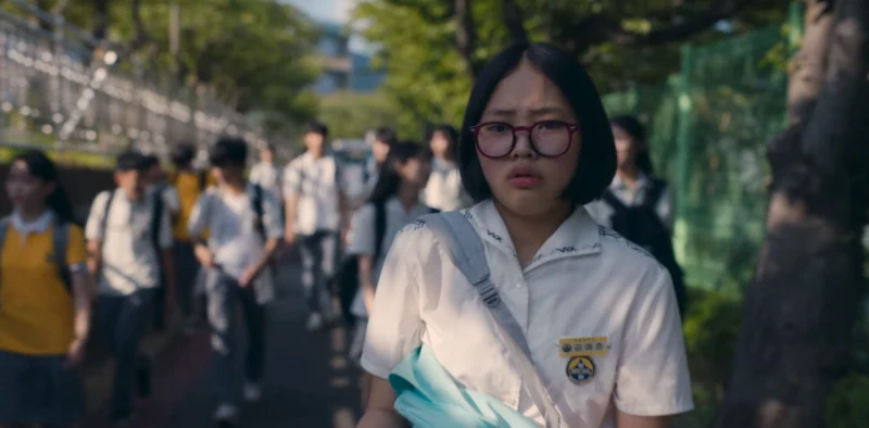 어느 학교 앞 학교하는 고등학생들을 배경으로 흰 교복을 입고 안경을 쓴 드라마 마스크걸의 김예춘