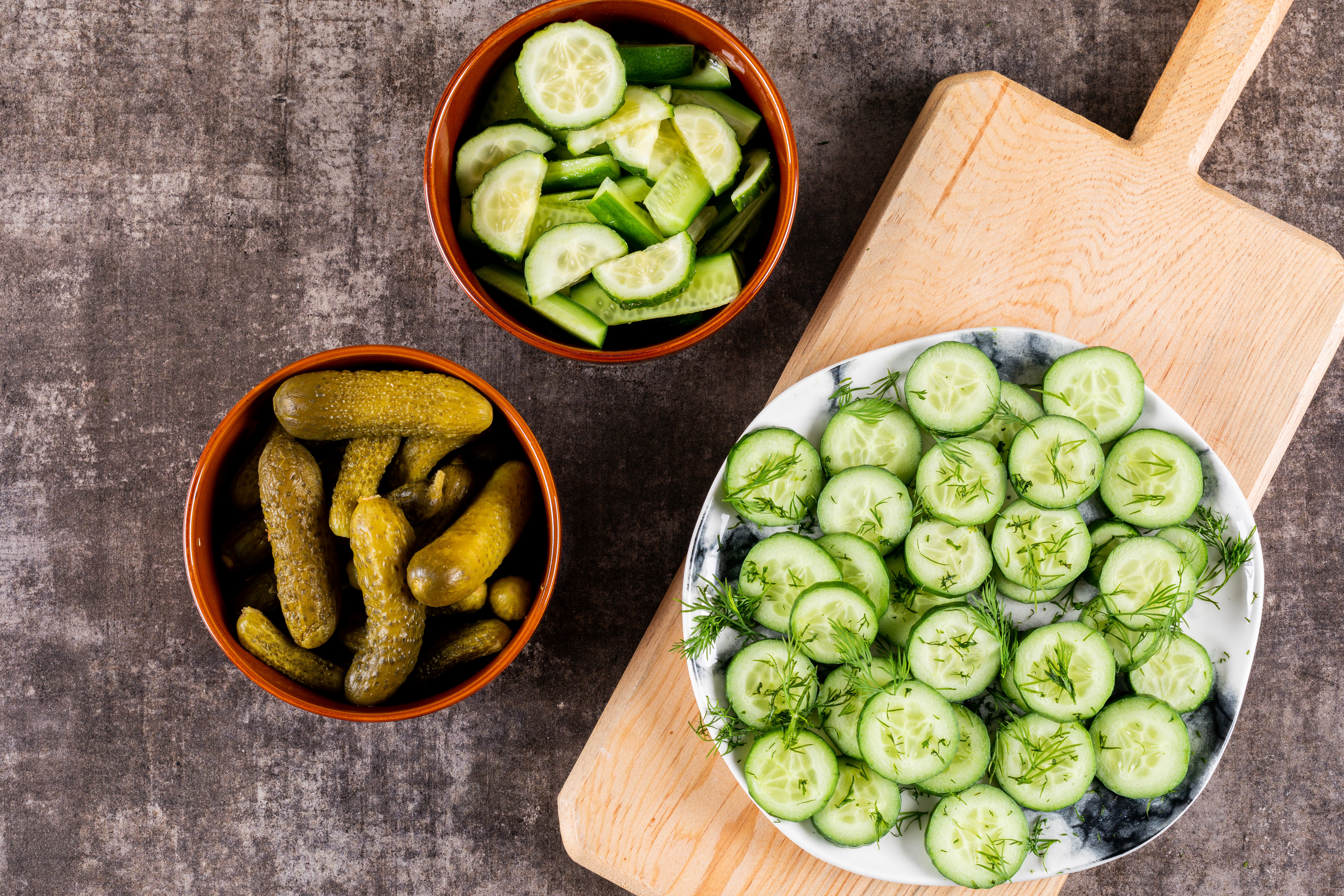 top-view-cucumber-fresh-sliced-with-dill-plate-wooden-cutting-board-pickled-bowl-brown-stone