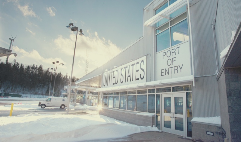 눈 덮인 미국 국경 입국심사소 건물 전경 – PORT OF ENTRY 표시와 함께 미국 입국 관문을 보여주는 풍경