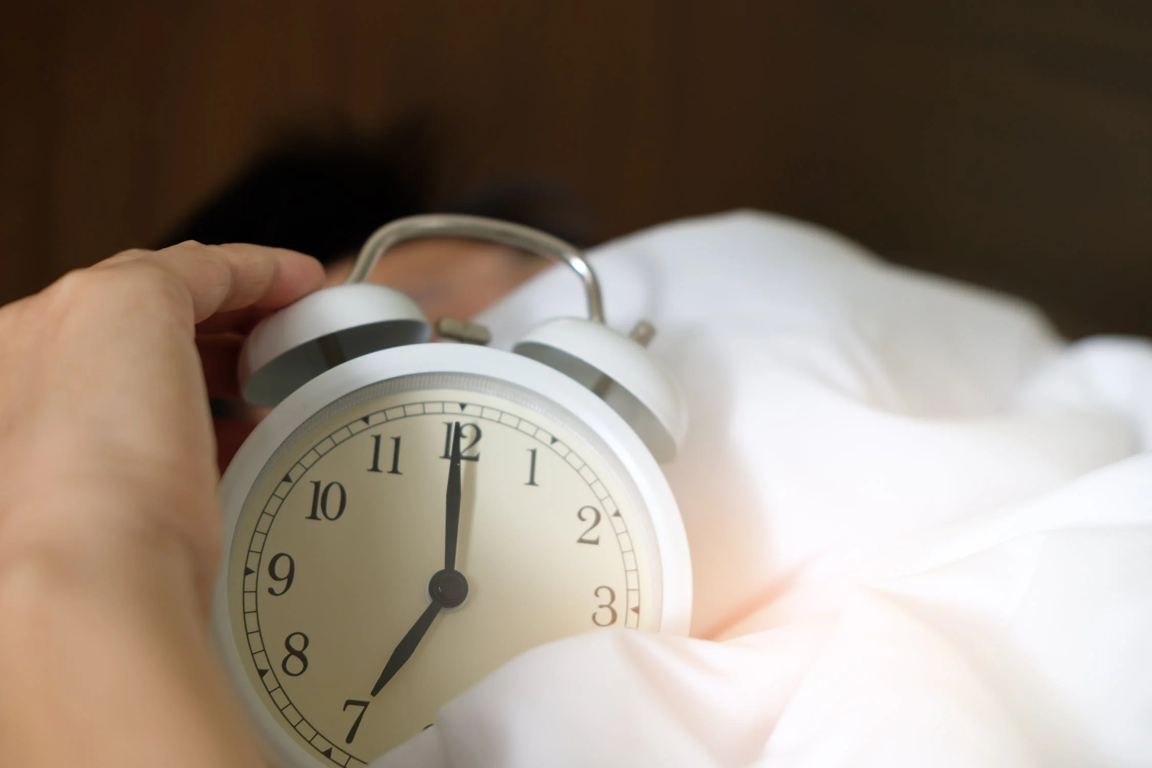 침대에서 어떤 사람이 자명종 시계를 끈채 다시 늦잠을 자고 있는 모습.