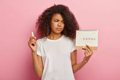 displeased-stressful-dark-skinned-woman-looks-periods-calendar-with-marked-red-crosses