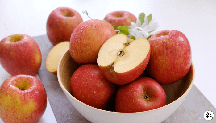 빨간 사과가 바닥과 흰 그릇에 담져있고 반쪽 사과도 한개 올려져있다