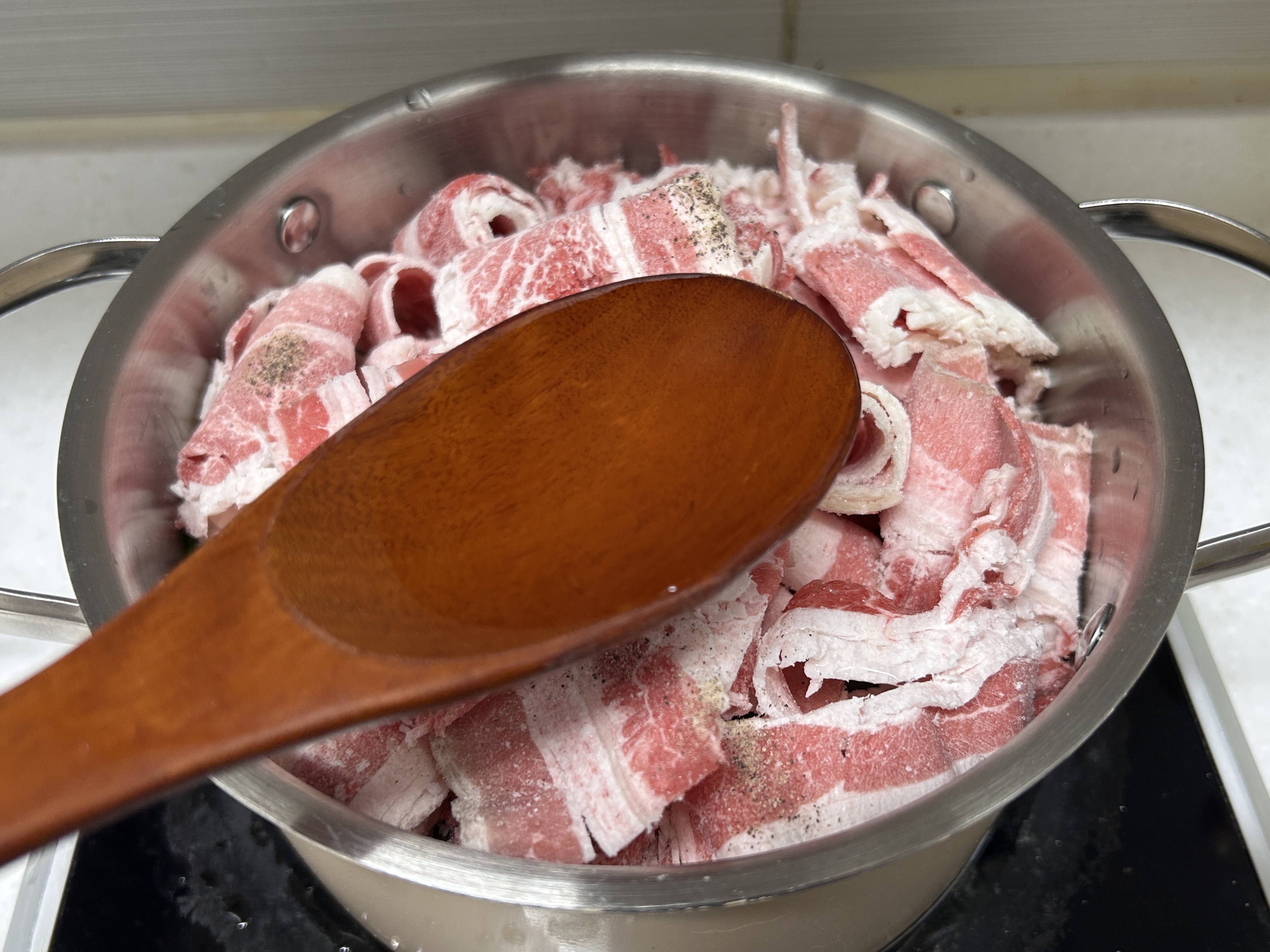 맛술로 한 숟갈 가득 채운 주걱 뒤로 우삼겹이 든 냄비가 보인다.