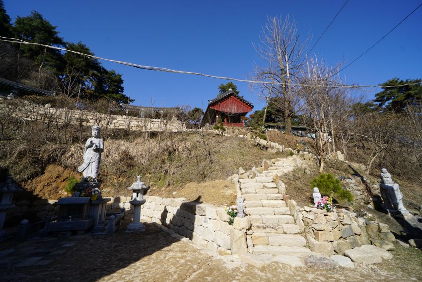 푸른 하늘&#44; 뒤 언덕으로 올라가는 돌계단&#44; 그 위에 사찰 건물들&#44; 왼쪽에 작은 석불상&#44; 석등&#44;