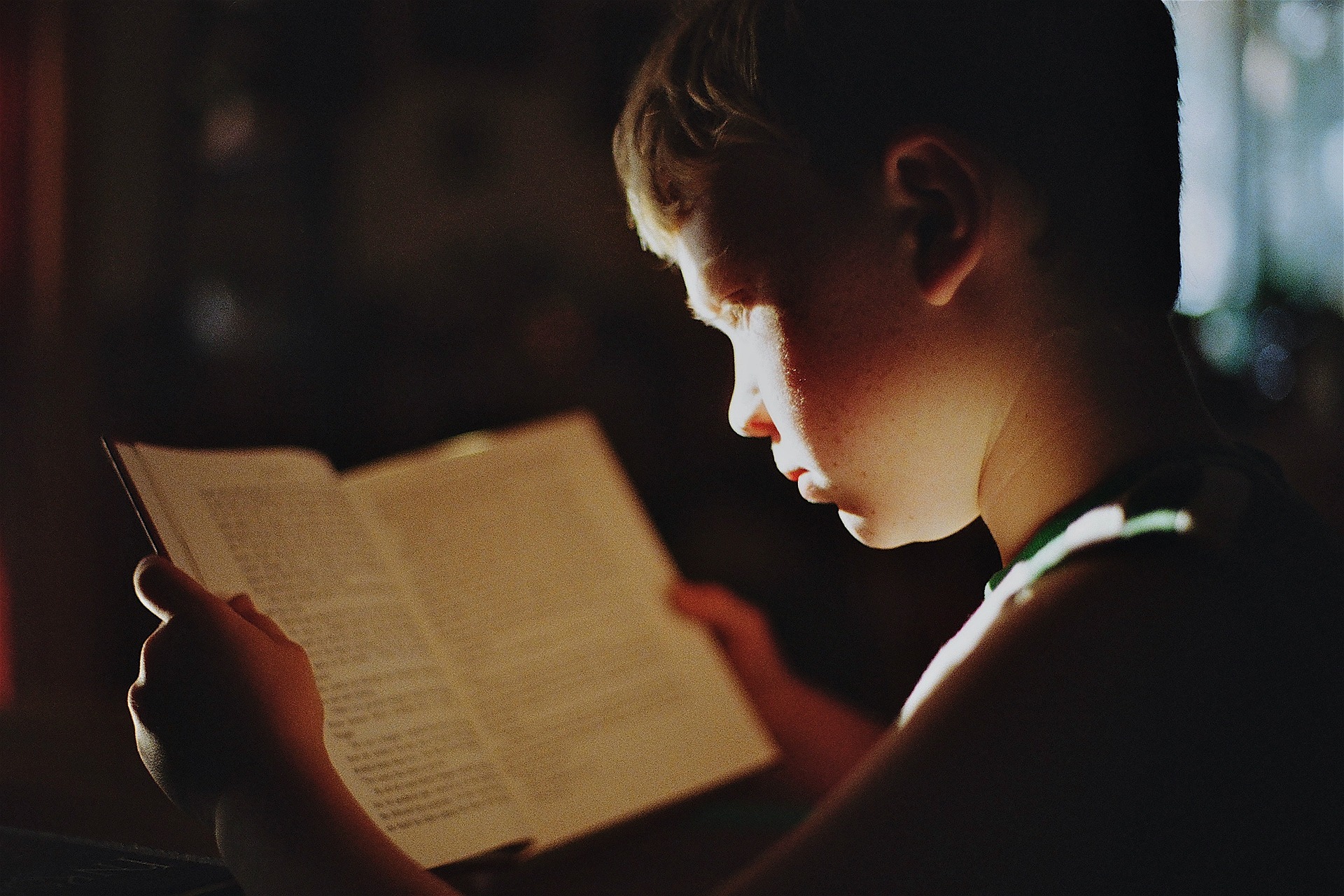 어두운 방에서 작은 불빛을 통해 책을 집중해서 읽고 있는 아이를 찍은 사진