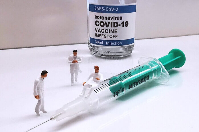covid 백신과 주사기, 그리고 작은 사람 모양의 피큐어 세개 놓여있는 모습