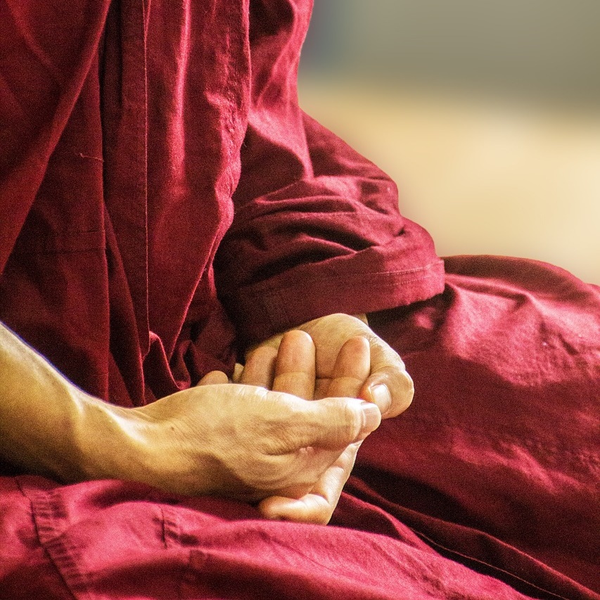 스님이 붉은 가사를 입고 양 손을 포갠채 앉아 있다.