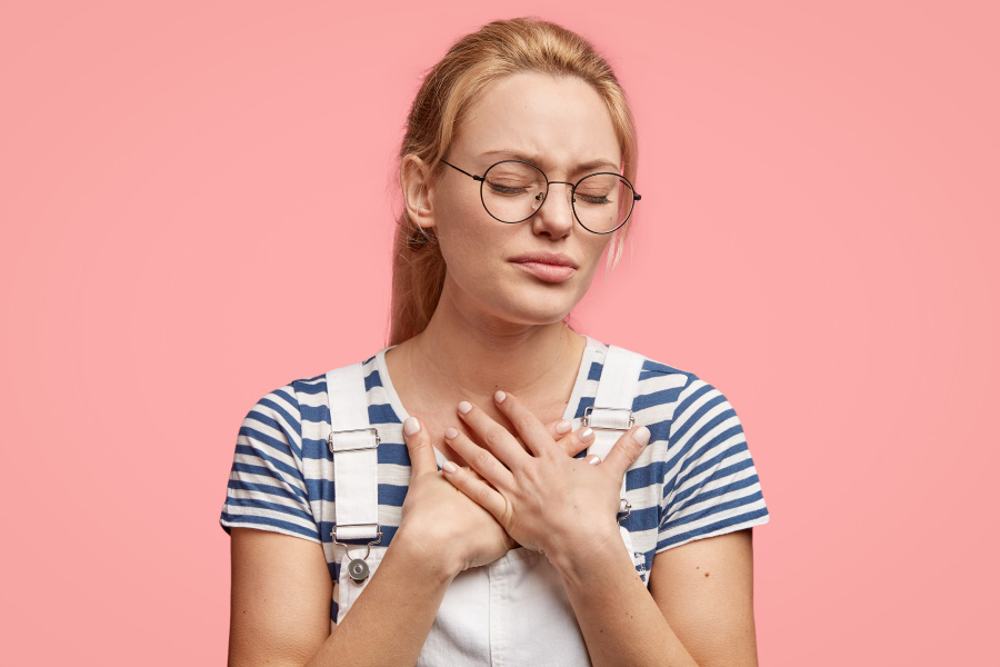 sad-stressful-young-caucasian-woman-keeps-hands-chest-feel-pain-heart-closes-eyes-stands-against-pink-wall