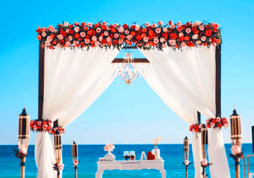 바다가 뒤로 보이는 해변에 결혼식 피로연이 설치됐다. 하얀 커튼이 양갈래로 묶여있고 위에는 빨간 장미, 분홍장미로 장식됐다.