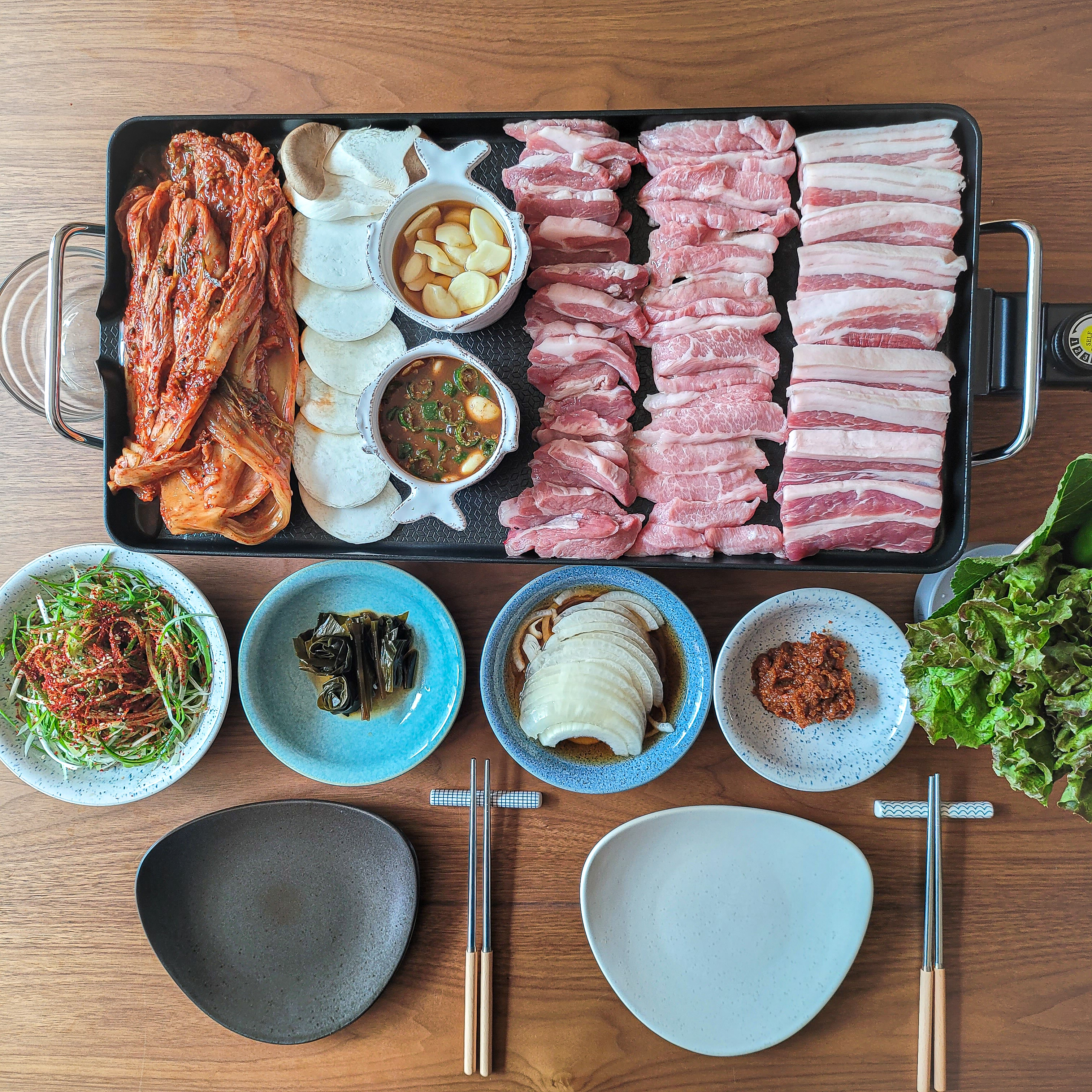그릴에 올린 돼지고기와 김치 그리고 각종 양념, 반찬, 상추, 깻잎들을 놓은 모습
