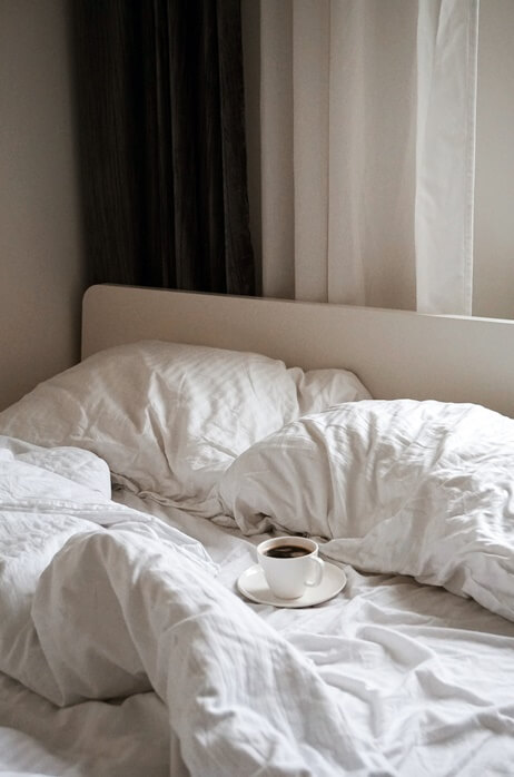 흰색 침구가 있는 침대 위에 차 한 잔이 놓여있는 모습