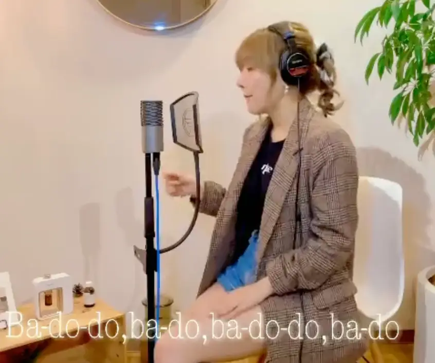 한일-갈색 벽 앞 스탠딩 마이크 앞 흰 의자에 앉아 노래하고 있는 마코토