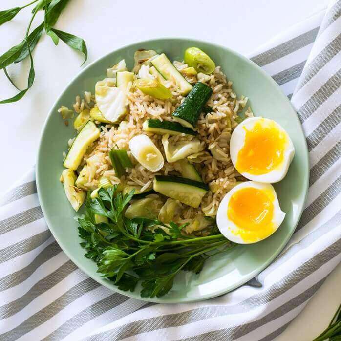 초록색 계통의 접시 위에 볶음밥과 오이&#44; 채소들&#44; 계란 반숙이 올려져 있는 모습