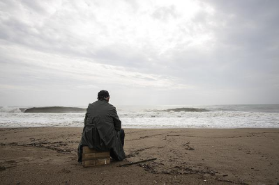 파도치는 바닷가 모래 위 의자에 앉아 있는 남자 노인 한 명