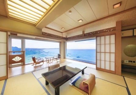 일본식 방에 테이블과 좌식 의자가 있고 창 밖으로 바다가 보인다.