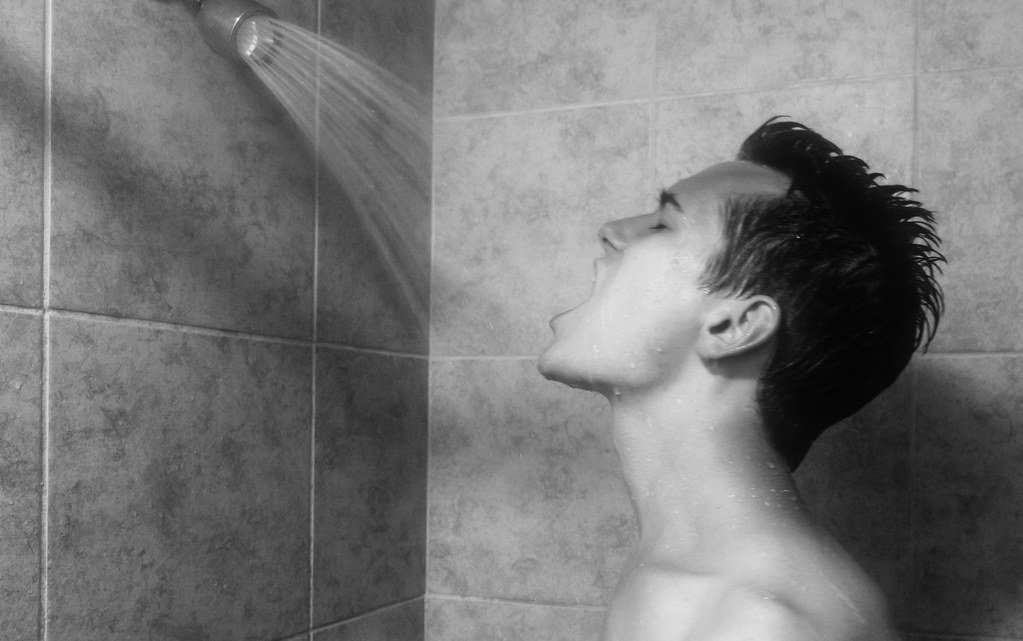 샤워를 하고있는 남자의 모습. 샤워기에서 물이 나오고 남자는 입을 벌리고 샤워기에서 나온 물을 먹고 있다.