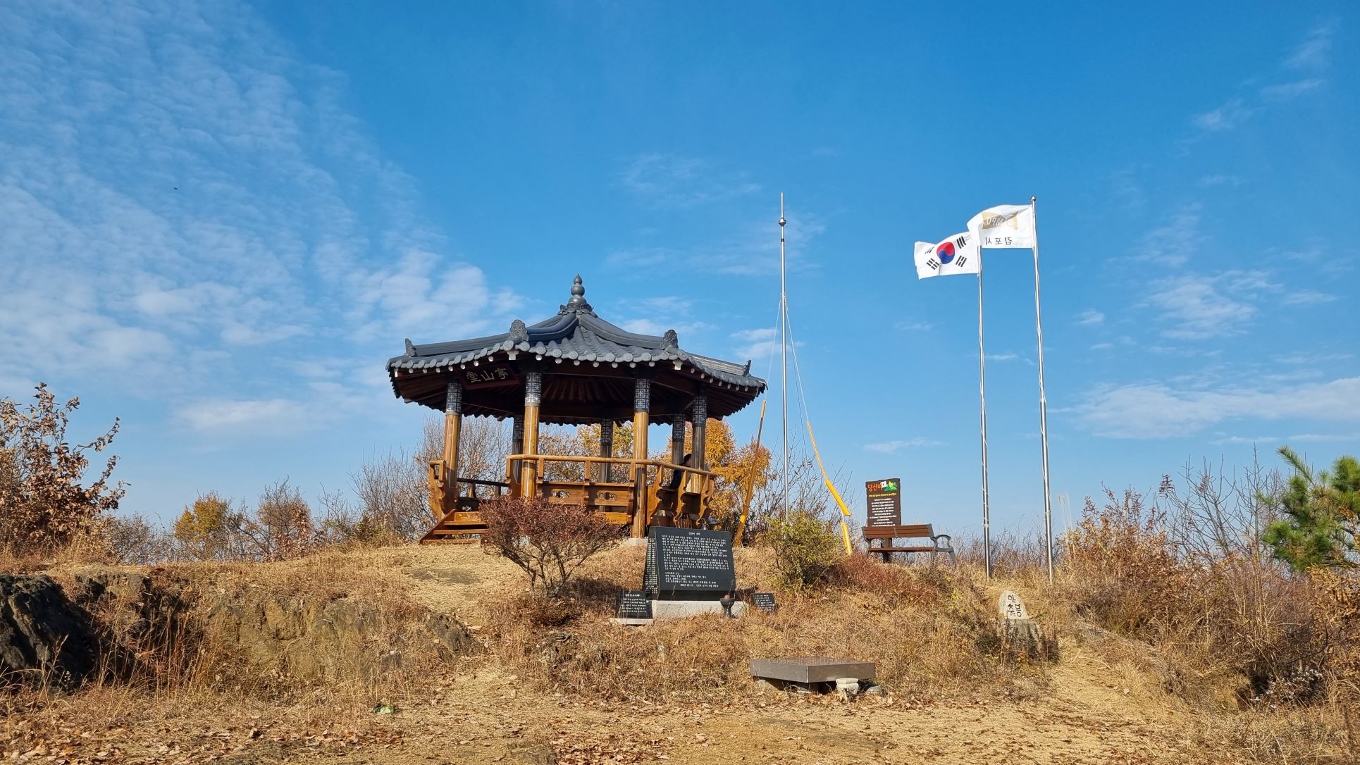 창공&#44; 푸른 하늘&#44; 나부끼는 태극기&#44; 김포시 깃발&#44; 가운데 팔각정 당산정&#44; 앞에 검은 비석 안내판&#44;