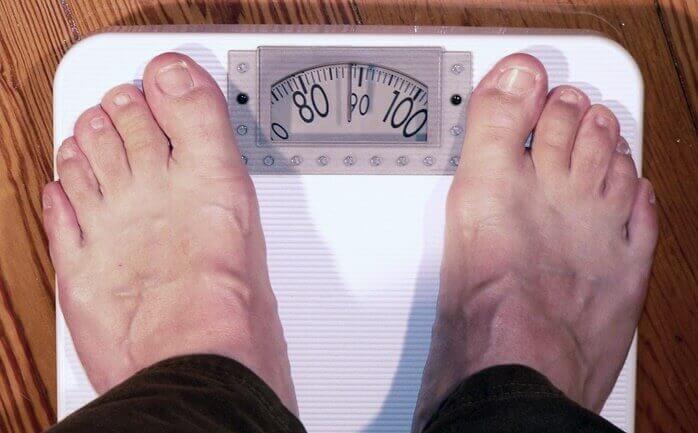 맨발의 남성이 올라가 있는 디지털 체중계의 바늘이 89kg를 가리키고 있는 모습