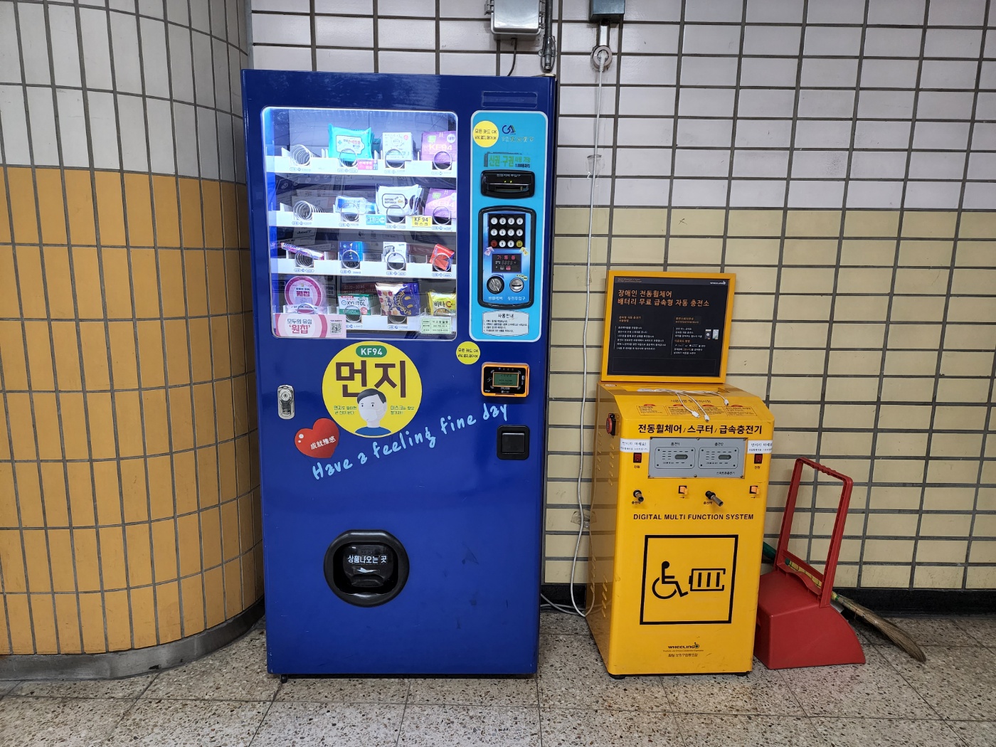 6호선 망원역 물품보관함 맞은편에 있는 파란색 생활용품 자판기&#44; 노란색 휠체어 충전기&#44; 청소용 빗자루와 쓰레받기