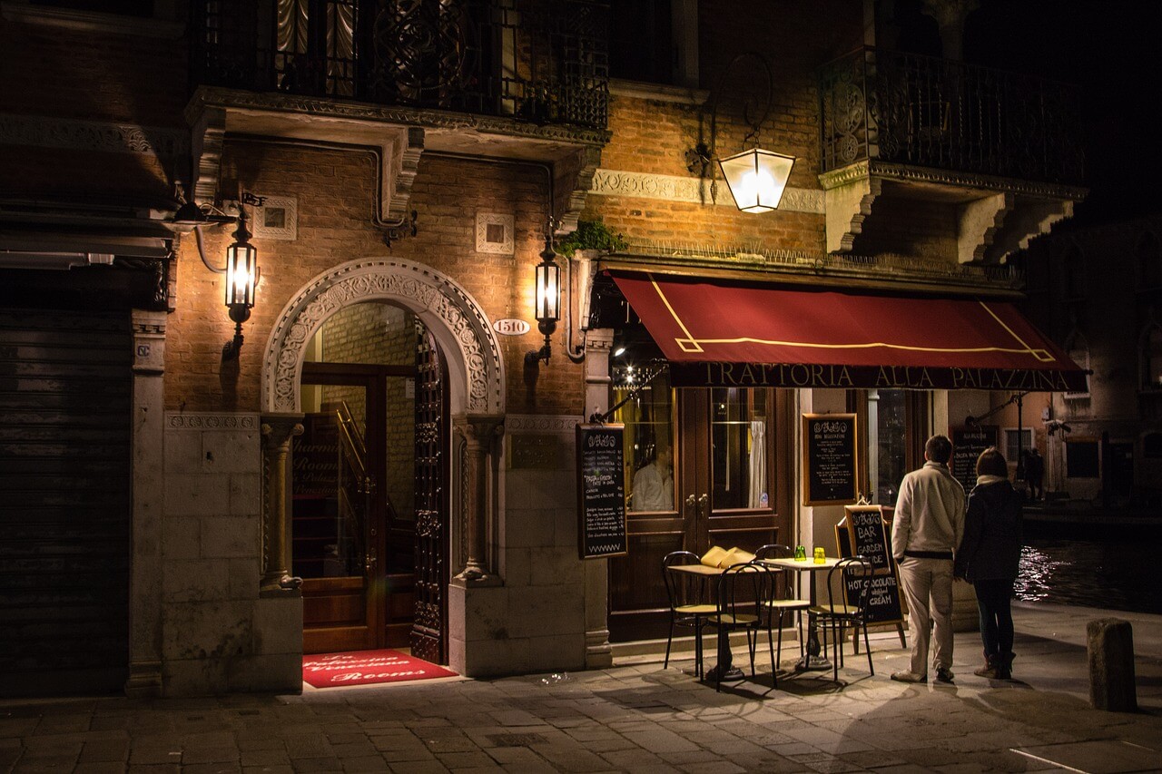 밤에 이탈리아의 한 식당 앞에 서 있는 두 사람
