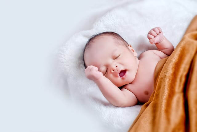 아기가 담요를 덮고 누워서 한쪽 팔을 들고 있는 모습