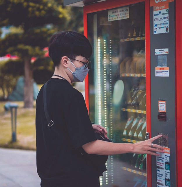 자판기에서 음료를 고르는 안경 낀 사람의 사진