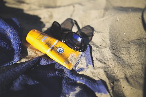 해변 모래사장에 있는 자외선 차단제와 선글라스 그리고 수건