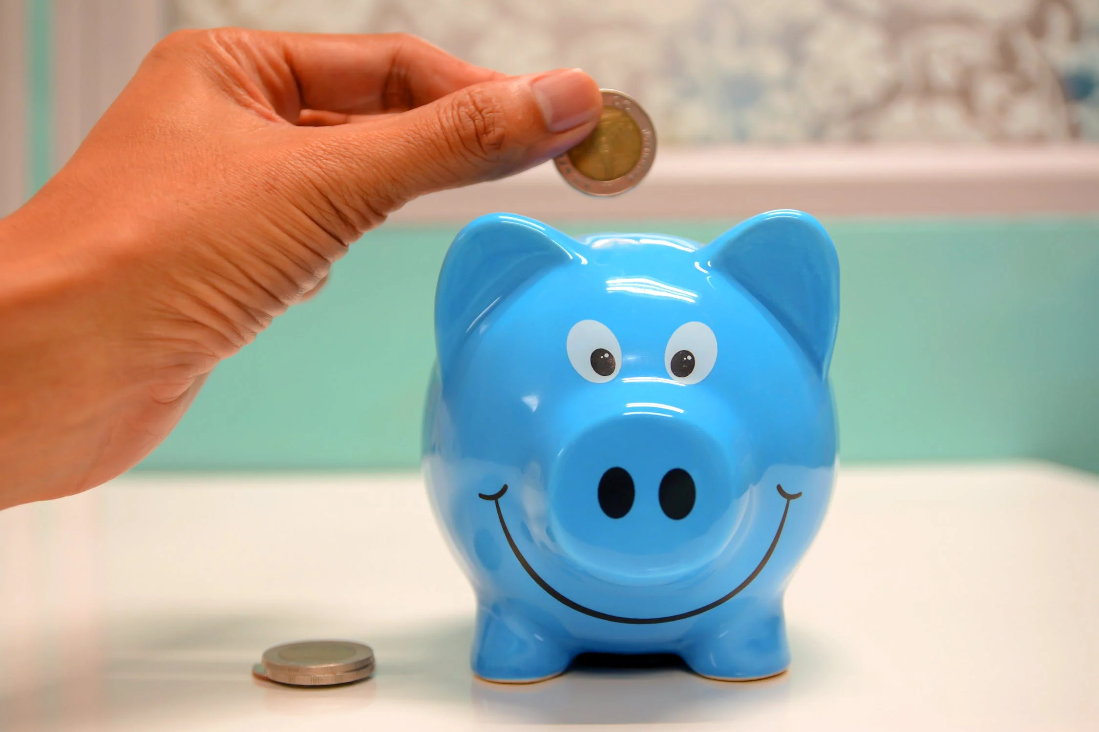 파란색 돼지 저금통에 동전을 넣고 있다.