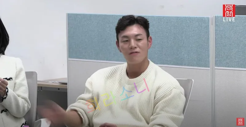 아이보리색 니트를 입은 남성이 흰 벽과 파란색 파티션이 있는 공간에서 팔을 들어 올리며 앉아 있다. 화면 오른쪽 상단에는 '촌장 LIVE' 로고가 보인다. 자막은 '희라소니'라고 적혀 있다.
