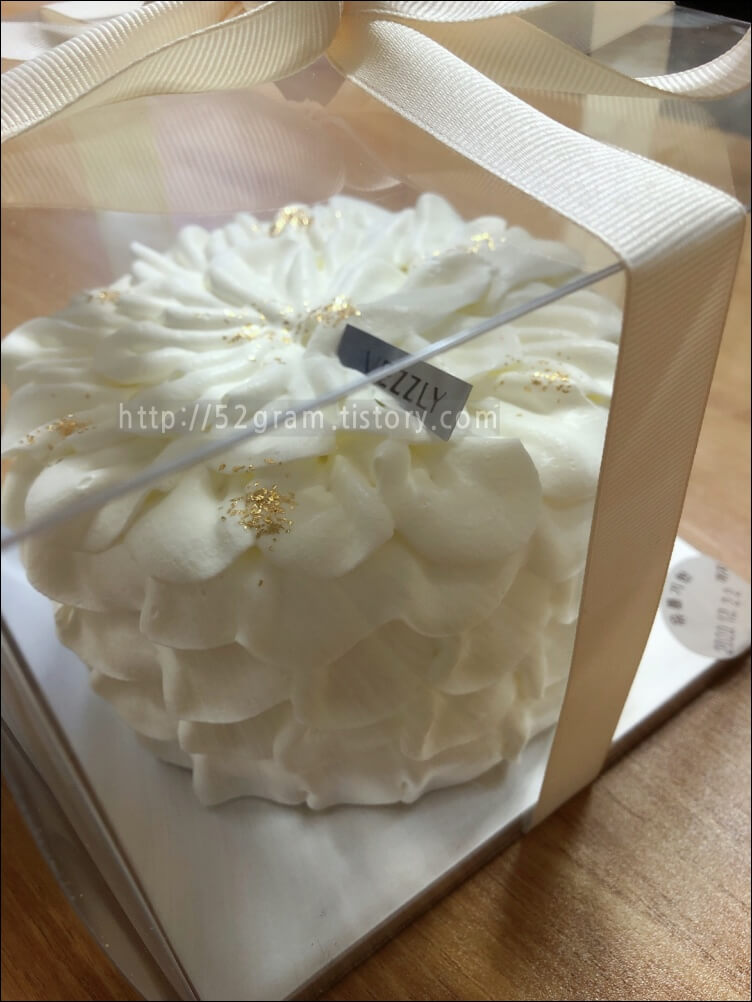 흰색 베즐리 케이크가 투명 상자 안에 담겨있다.