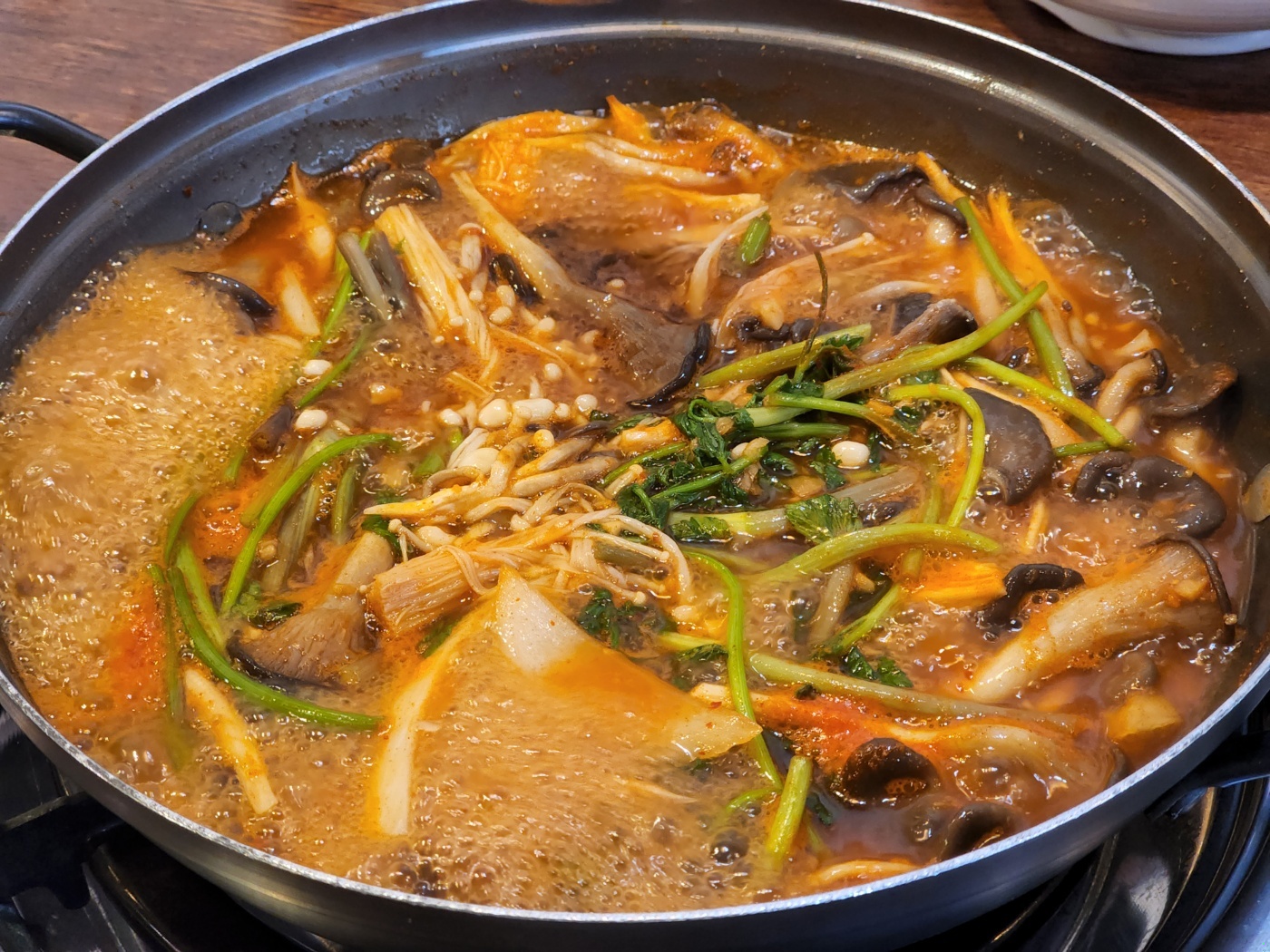 팽이버섯, 미나리, 감자, 양파 등 버섯 매운탕의 속재료들이 빨간 매운탕 국물 속에서 팔팔 끓고 있는 사진
