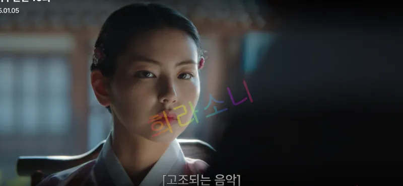 소혜 아씨가 단정하게 빗어 올린 머리를 하고 정면을 응시하고 있습니다. 그녀는 담담한 표정으로 앉아 있으며&amp;#44; 자막은 &amp;quot;[고조되는 음악]&amp;quot;.