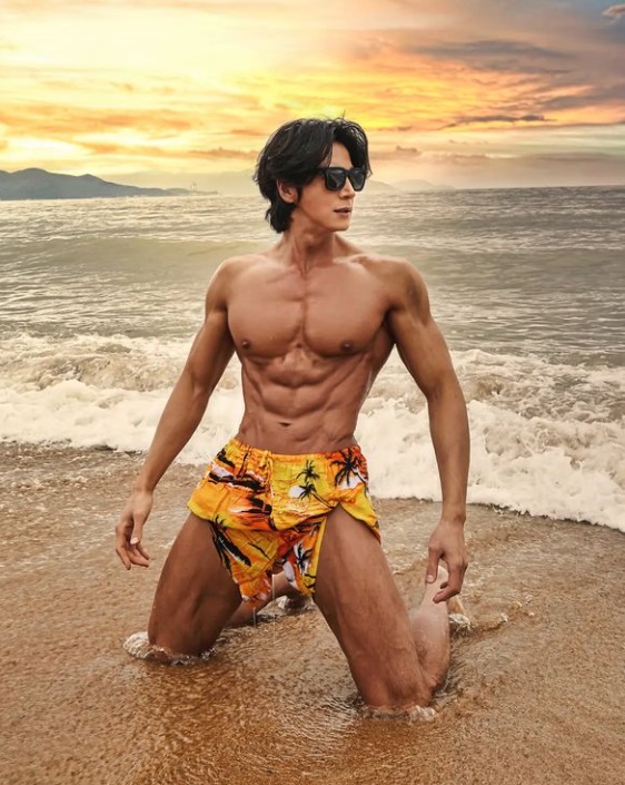 이국용이 해변 모래사장에 검은 선글라스를 착용한 반바지이지만 신체의 근육을 보여 무릎을 꿇은 자세 사진