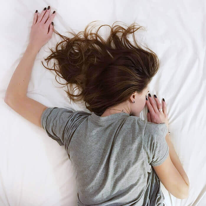 회색 반팔 티를 입은 금발의 여자가 침대에 엎드린 포즈로 자고 있는 모습