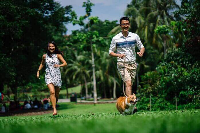 남녀가 반려견과 함께 잔디밭 위를 웃으며 달리고 있는 모습