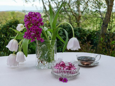 테이블 위 튤립과 자주색 꽃이 꽂혀 있는 유리병과 차 한잔이 있는 야외 정원 풍경