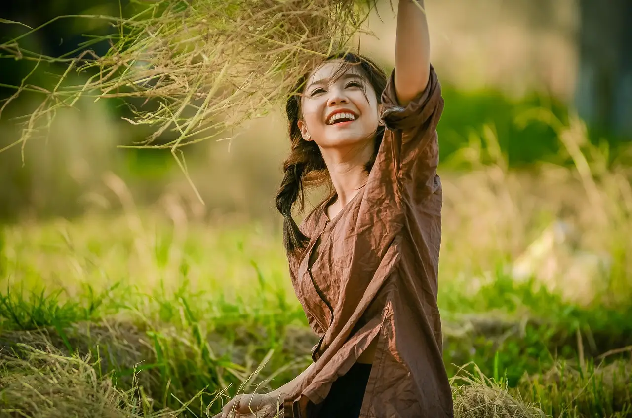 청년수당- 초록 풀밭위 갈색옷을 입은 여자가 웃으며 나뭇잎을 만지는 모습