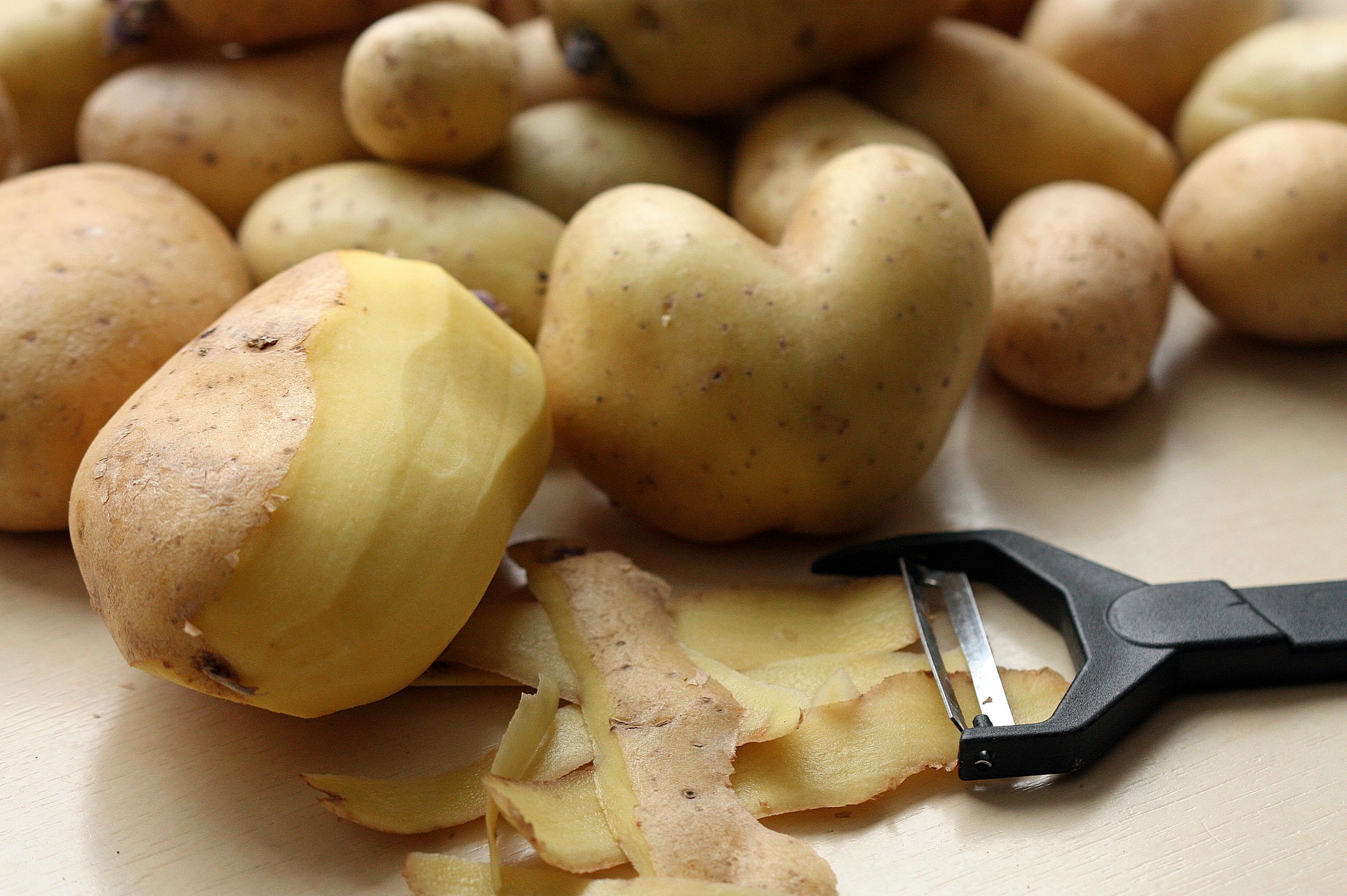바닥에 감자를 많이 놓아두고&#44; 그 중에서 1개는 감자를 깎는 칼로 반쯤 껍질을 까 놓은 사진