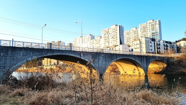 푸른 하늘&#44; 아파트 건물들&#44; 아치형 교량 하단에 비치는 노란 석양빛&#44;