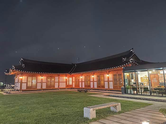 검은 밤 하늘을 배경으로 경주 한옥숙소 화랑루 전체에 조명이 켜지고 마당의 잔디가 보이는 사진