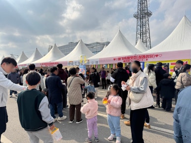 여러 개의 흰색 천막 부스 앞에서 줄을 서 있는 방문객들.