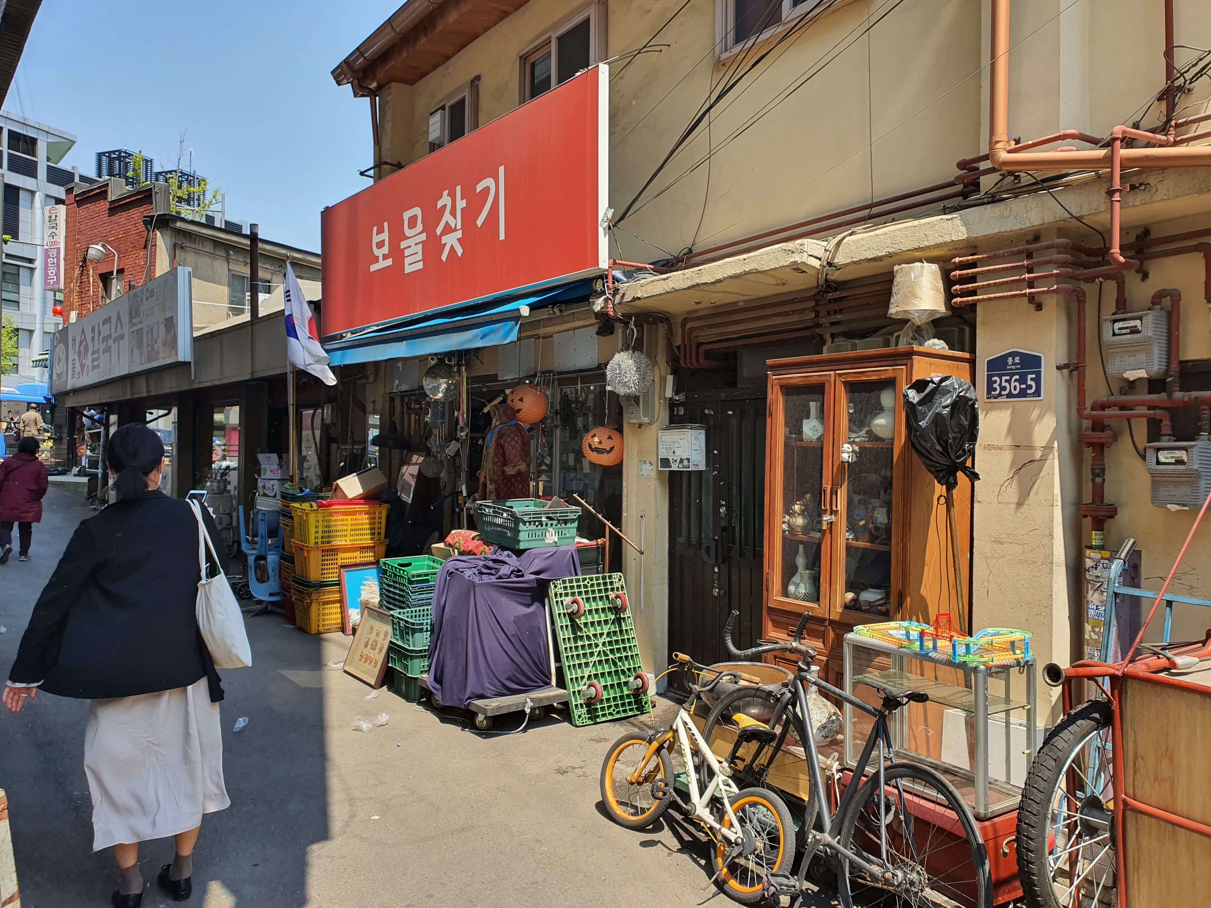 오래된 물건들이 보물찾기라는 상점 앞에 놓여져 있다 빨간 간판의 하얀 글씨인 보물찾기 상점이 오른편에 보인다.