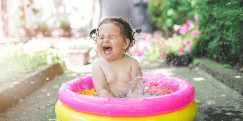 노란색 핑크색 튜브에 여자아기가 물놀이 하며 웃는 사진