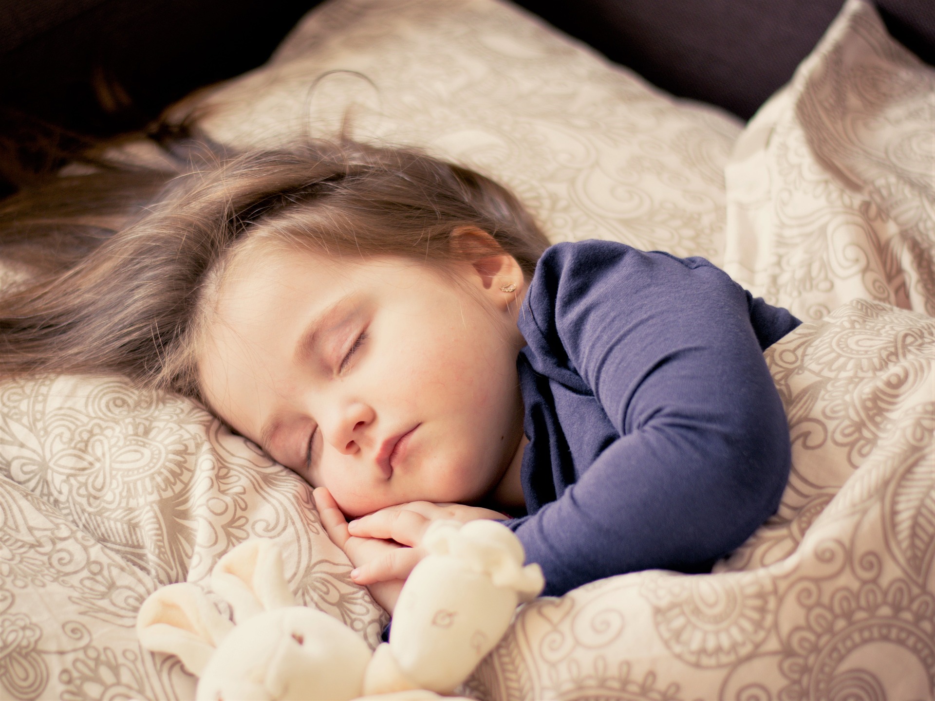 침대에서 옆으로 누워 인형을 옆에 두고 곤히 잠을 잘 자고 있는 어린아이 사진