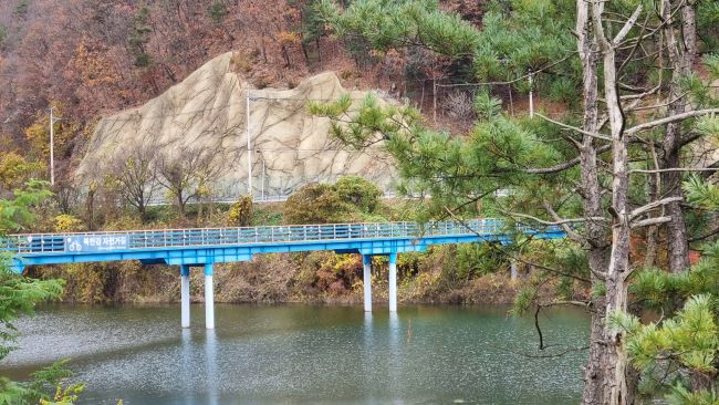 의암호를 넘어 신매대교 쪽으로 가는 하늘색 다리&#44; 우측엔 키 큰 소나무들&#44; 다리 건너편엔 거대한 흰색 바위 절벽&#44;