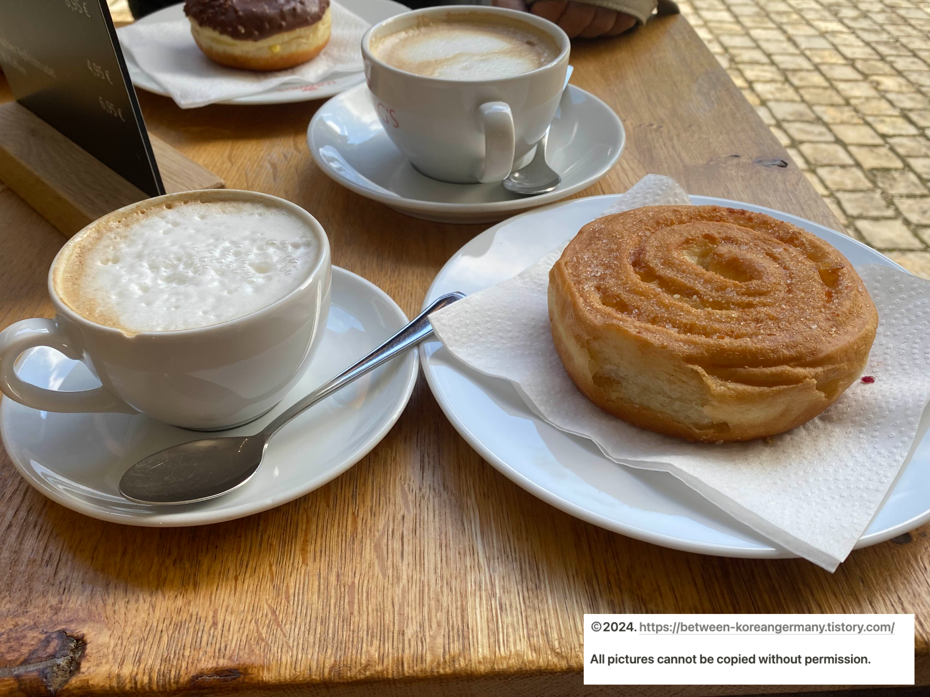 흰색 커피잔에 담겨있는 두 잔의 카푸치노와 그 옆에 놓인 설탕이 뿌려진 도넛&#44; 그리고 초콜렛이 입혀진 도넛