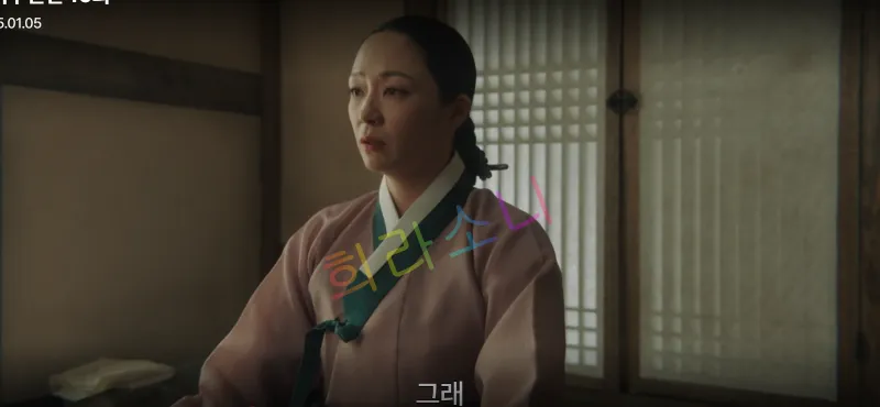 분홍빛 한복을 입은 송씨부인이 방 안에서 진지한 표정으로 앉아 있습니다. 그녀의 뒤로는 전통 창살 무늬가 보입니다. 자막은 &amp;quot;그래.&amp;quot;