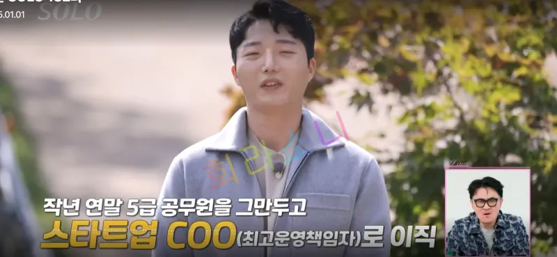 24기 광수가 야외에서 인터뷰를 진행하고 있다. 그는 밝은 회색 재킷을 입고 있다. 화면 하단에는 